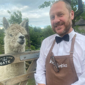 Dave from Vegan Junkies in bow tie and branded apron at a UK wedding venue with an alpaca
