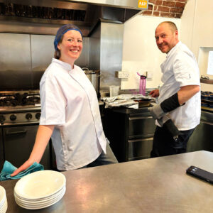 Sophie and Dave from Vegan Junkies in chef whites preparing food in a professional kitchen