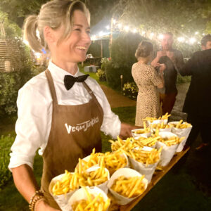 Vegan Junkies server carrying evening food chips in cones at a UK wedding under festival lights