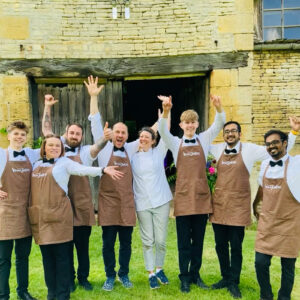 A Vegan Junkies wedding catering team in branded aprons and bow ties celebrating at a UK wedding venue